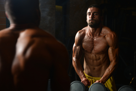 Portrait Of A Young Muscular Athletic Man Posing While Sitting And Showing Bodybuilding Pose In Modern Fitness Centerの写真素材