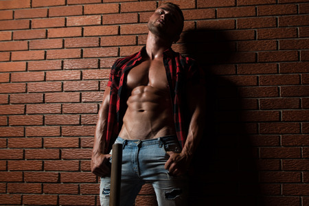 Portrait Of A Young Physically Fit Man Showing His Well Trained Body While Wearing Plaid Shirt - Muscular Athletic Bodybuilder Fitness Model Posing After Exercises On Wall of Bricksの写真素材