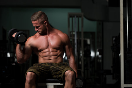 Healthy Man Working Out Biceps In A Dark Gym - Dumbbell Concentration Curls