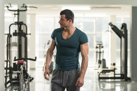 Healthy Young Man in Green T-shirt Standing Strong and Flexing Muscles - Muscular Athletic Bodybuilder Fitness Model Posing After Exercisesの写真素材