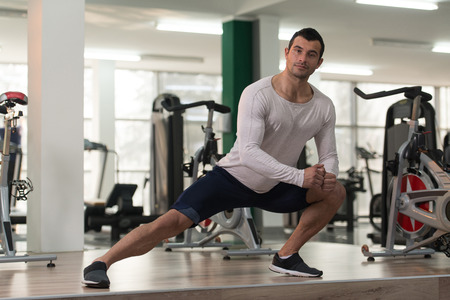 Muscular Man Stretches At The Floor In A Gym And Flexing Muscles - Muscular Athletic Bodybuilder Fitness Modelの写真素材