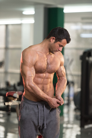 Hairy Healthy Young Man Standing Strong In The Gym And Flexing Muscles - Muscular Athletic Bodybuilder Fitness Model Posing After Exercisesの写真素材