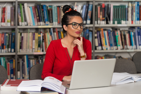 In The Library - Pretty Female Student With Laptop And Books Working In A High School Or University Library - Shallow Depth Of Fieldの写真素材