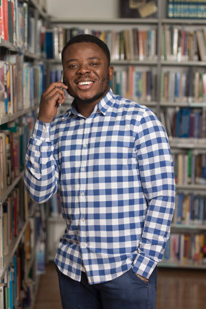 African Male Student Talking On The Phone In Library - Shallow Depth Of Field