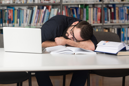 Sleeping Caucasian Student Sitting And Leaning On Pile Of Books In College - Shallow Depth Of Fieldの写真素材