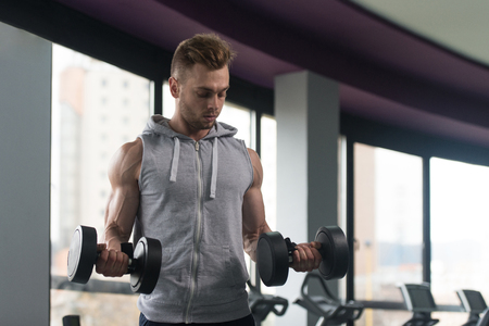 Young Man Working Out Biceps In Gym - Dumbbell Concentration Curlsの写真素材