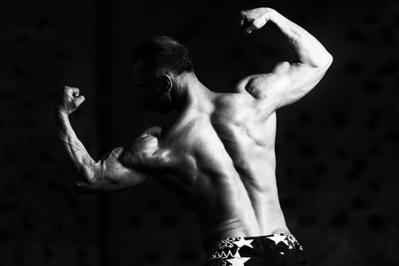 Healthy Young Man Standing Strong In The Gym And Flexing Muscles - Muscular Athletic Bodybuilder Fitness Model Posing After Exercisesの写真素材