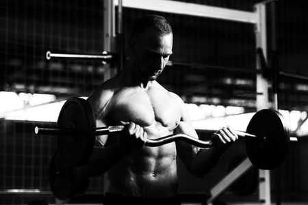 Muscular Man Doing Heavy Weight Exercise For Biceps With Barbell In Gymの写真素材