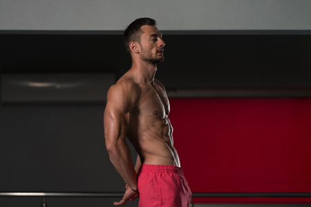 Healthy Young Man Standing Strong In The Gym And Flexing Muscles - Muscular Athletic Bodybuilder Fitness Model Posing After Exercisesの写真素材