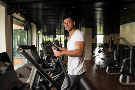 Muscular Man Doing Aerobics Elliptical Walker In Modern Fitness Centerの写真素材