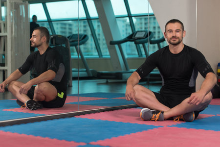 Muscular Man Stretches At The Floor In A Gym And Flexing Muscles - Muscular Athletic Bodybuilder...