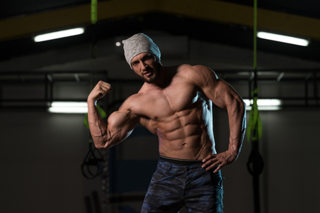 Healthy Young Man Standing Strong In The Gym And Flexing Muscles - Muscular Athletic Bodybuilder Fitness Model Posing After Exercisesの写真素材