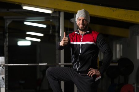 Portrait Of A Physically Fit Man In Track Suit Resting His Well Trained Body Showing Thumbs Up - Muscular Athletic Bodybuilder Fitness Model Posing After Exercisesの写真素材