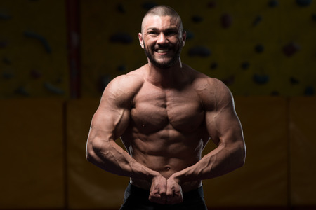 Healthy Young Man Standing Strong In The Gym And Flexing Muscles - Muscular Athletic Bodybuilder Fitness Model Posing After Exercisesの写真素材