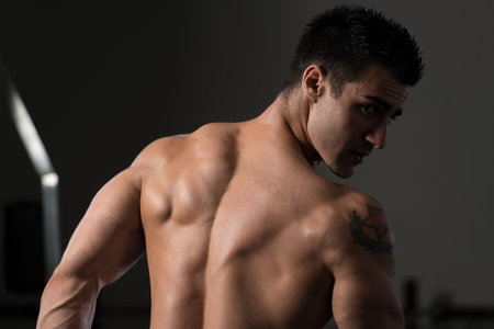 Handsome Man Standing Strong In The Gym And Flexing Muscles - Muscular Athletic Bodybuilder Fitness Model Posing After Exercisesの写真素材