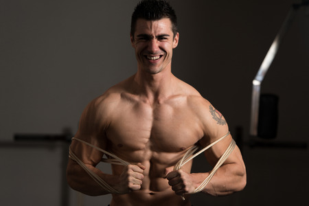 Handsome Man Standing Strong In The Gym And Flexing Muscles With Cable - Muscular Athletic Bodybuilder Fitness Model Posing After Exercisesの写真素材
