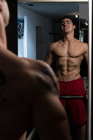 Handsome Man Standing Strong In The Gym And Flexing Abdominal Muscles - Muscular Athletic Bodybuilder Fitness Model Posing After Exercisesの写真素材