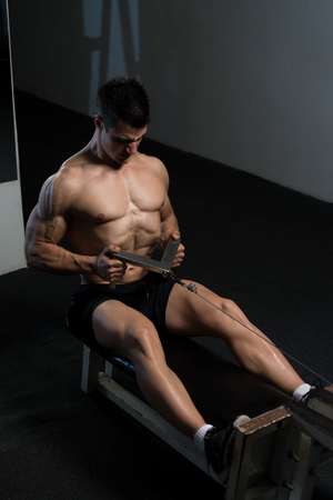 Strong Man In The Gym And Exercising Back On Machine - Muscular Athletic Bodybuilder Fitness Model Exerciseの写真素材