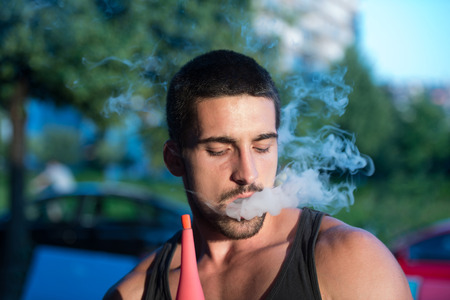 Young Man Smoking Shisha Outdoors - Man Exhaling Smoke Inhaling From A Hookahの写真素材