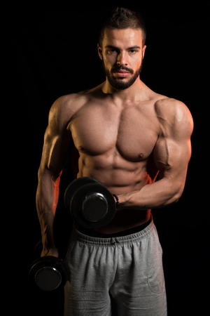 Muscular Model Doing Heavy Weight Exercise For Biceps With Dumbbells On Black Backgroundの写真素材