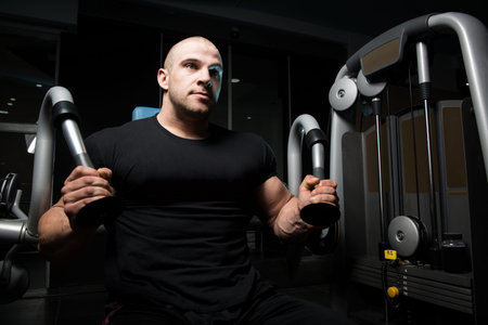 Young Muscular Fitness Bodybuilder Doing Heavy Weight Exercise For Triceps On Machine In The Gym