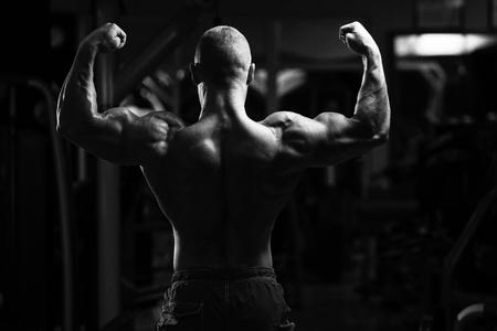 Healthy Young Man Standing Strong In The Gym And Flexing Muscles - Muscular Athletic Bodybuilder Fitness Model Posing After Exercisesの写真素材
