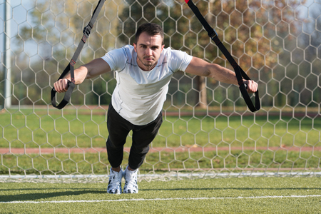 Attractive Man Doing Crossfit With Trx Fitness Straps in City Park Area - Training and Exercising for Endurance - Healthy Lifestyle Concept Outdoorの写真素材