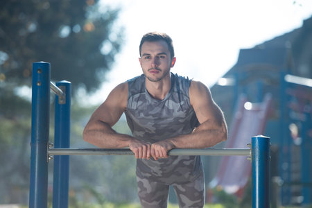 Young Man Doing Crossfit Exercise With Dips Bar in City Park Area - Training and Exercising for...