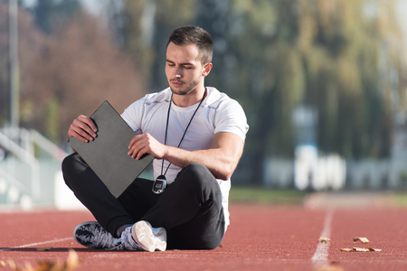 Personal Trainer In Sports Outfit Takes Notes On Clipboard in City Park Area - Training and Exercising for Endurance - Healthy Lifestyle Concept Outdoorの写真素材