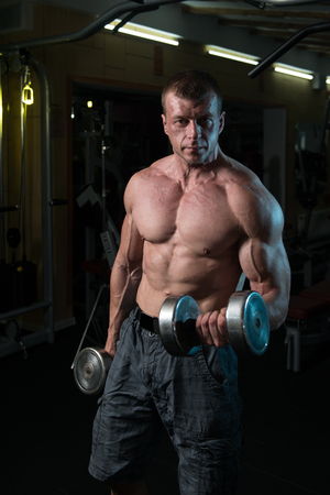 Muscular Man Doing Heavy Weight Exercise For Biceps With Dumbbells In Modern Fitness Center Gymの写真素材