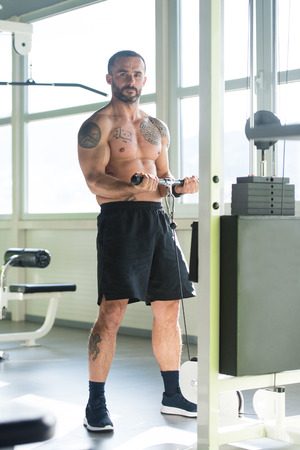 Muscular Fitness Bodybuilder Doing Heavy Weight Exercise For Biceps On Machine With Cable In The Gymの写真素材