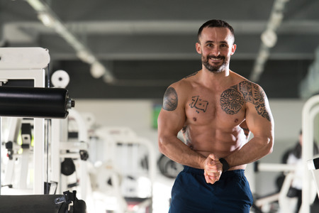 Handsome Young Man Standing Strong In The Gym And Flexing Muscles - Muscular Athletic Bodybuilder Fitness Model Posing After Exercisesの写真素材