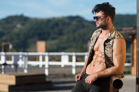 Handsome Cowboy Man Standing Strong and Posing at Ranch Outdoors Wearing Black Jeans - Background of Sky and Mountainsの写真素材