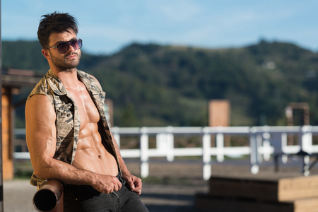 Handsome Cowboy Man Standing Strong and Posing at Ranch Outdoors Wearing Black Jeans - Background of Sky and Mountainsの写真素材