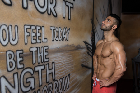 Portrait of a Young Physically Fit Man in White T-shirt Showing His Well Trained Body - Muscular Athletic Bodybuilder Fitness Model Posing After Exercises In Front Of A Graffiti Wallの写真素材