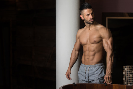 Healthy Young Man Standing Strong In Hot Sauna And Flexing Muscles - Muscular Athletic Bodybuilder Fitness Model Posing After Exercisesの写真素材