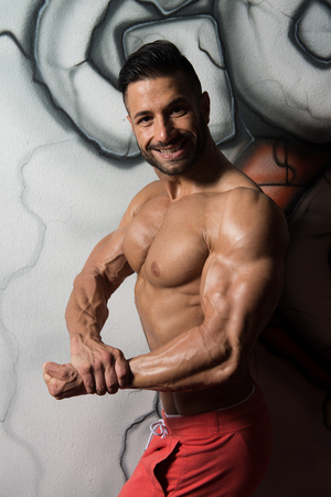 Portrait of a Young Physically Fit Man in White T-shirt Showing His Well Trained Body - Muscular Athletic Bodybuilder Fitness Model Posing After Exercises In Front Of A Graffiti Wallの写真素材