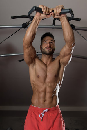 Young Muscular Fitness Bodybuilder Doing Heavy Weight Exercise For Triceps On Machine In The Gym