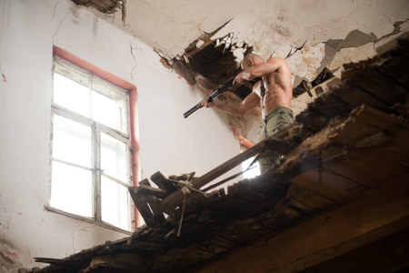 Action Hero Muscled Man Holding Machine Gun - Standing In Abandoned Building Wearing Army Pantsの写真素材