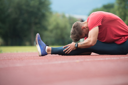 Sporty Man Stretching and Warming Up Legs for Running Fitness Workout on Track Exercising Outsideの写真素材