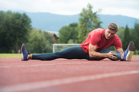 Sporty Man Stretching and Warming Up Legs for Running Fitness Workout on Track Exercising Outsideの写真素材