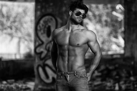 Portrait of a Young Physically Fit Man Showing His Well Trained Body - Muscular Athletic Bodybuilder Fitness Model Posing After Exercises In Front Of A Graffiti Wallの写真素材