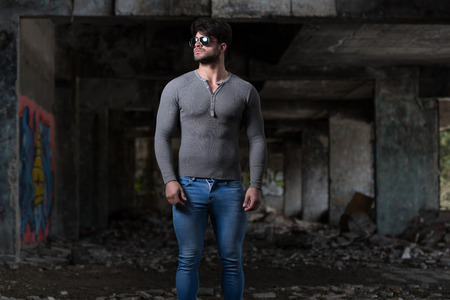 Portrait of a Young Physically Fit Man in Grey Long Sleeve Shirt Showing His Well Trained Body - Muscular Athletic Bodybuilder Fitness Model Posing After Exercises In Front Of A Graffiti Wallの写真素材