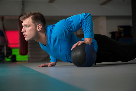 Handsome Young Man Doing Pushups With Medicine Ball As Part Of Bodybuilding Trainingの写真素材
