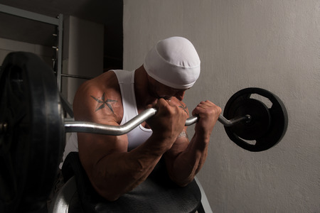 Muscular Man Doing Heavy Weight Exercise For Biceps With Barbell In Gymの写真素材