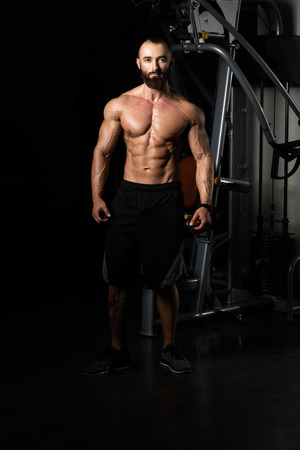 Handsome Young Man Standing Strong In The Gym And Flexing Muscles - Muscular Athletic Bodybuilder Fitness Model Posing After Exercisesの写真素材
