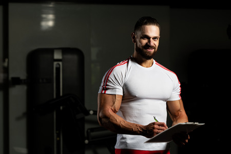 Personal Trainer Takes Notes On Clipboard In Fitness Center Gymの写真素材