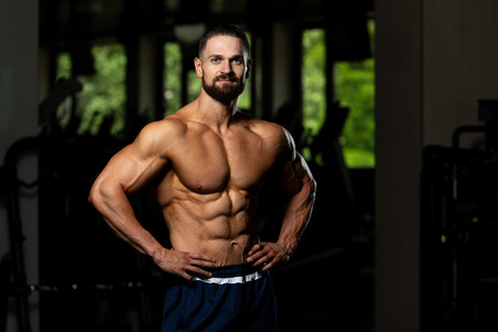 Young Man Standing Strong In The Gym And Flexing Muscles - Muscular Athletic Bodybuilder Fitness Model Posing After Exercisesの写真素材