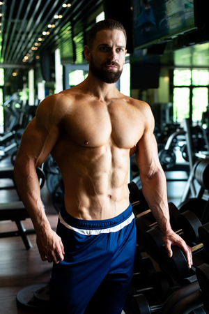 Handsome Young Man Standing Strong In The Gym And Flexing Muscles - Muscular Athletic Bodybuilder Fitness Model Posing After Exercisesの写真素材