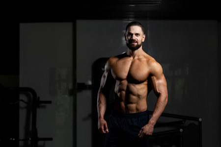 Young Man Standing Strong In The Gym And Flexing Muscles - Muscular Athletic Bodybuilder Fitness Model Posing After Exercisesの写真素材